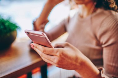 Sıradan giyinen çiftçi kadın, akıllı telefon kullanarak sosyal medya mesajları yazarak kafede rahat rahat oturuyor. 