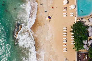 Açık havuzu ve güneş pansiyonları olan ilk hat plaj otelinin havadan görünüşü. Yaz tatillerinin kuş bakışı manzarası, turkuaz deniz suyu ve temiz kum kıyısındaki şemsiyeler.