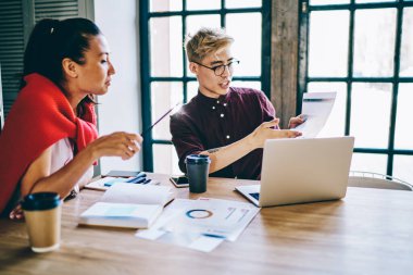 Gündelik kıyafetlerle birbirleriyle sohbet eden ve ofisteki yaratıcı iş yerlerindeki grafikleri analiz eden ciddi çeşitlilikte genç iş arkadaşları.