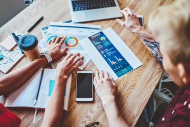 İş arkadaşlarının üstlerinden, günlük giysiler içinde dizüstü bilgisayarlı cep telefonu fincanı ile masada oturup iş yerinde tartıştıkları.