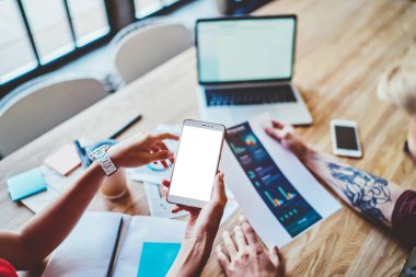 İş arkadaşlarının üstlerinden, günlük kıyafetlerini giymiş, dizüstü bilgisayarla masaya oturmuş, cep telefonlarını analiz ediyor, iş yerinde tartışmalar yapıyor. 
