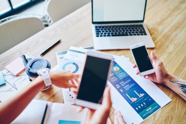 İş arkadaşlarının üstlerinden, günlük giysiler içinde dizüstü bilgisayarlı kahve fincanı ve cep telefonuyla çalışma alanında tartışmaları.
