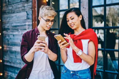 Mutlu gülümseyen Asyalı çift günlük giysiler içinde beyaz tişörtler giyip yazın sokakta cep telefonlarını izliyorlar.