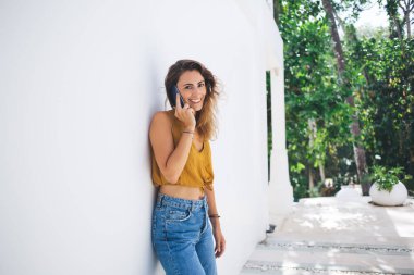 Cep telefonuyla konuşan kıvırcık bir kadın büyüleyici bir gülümseme ile uçsuz bucaksız bir evin bahçesinde bitkilerle ve yeşilliklerle dolanıyor. 