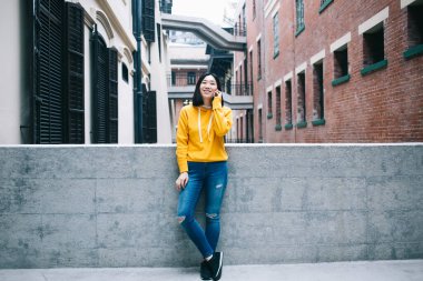 Kot pantolon ve sweatshirt giyen genç Asyalı kadın beton çitin yanında dikiliyor ve yüzünü çeviriyor.