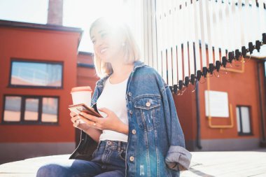 Kot pantolon ve beyaz t-shirt 'lü, gülümseyen sarışının kahve fincanı içerken cep telefonunda arka koltukta otururken.