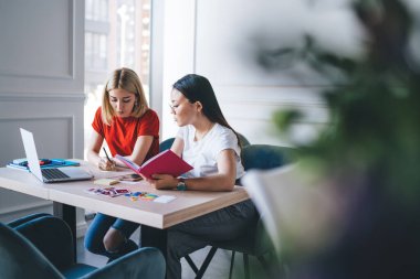 Genç ve zeki odaklı, gündelik giysiler içinde dizüstü bilgisayarla çalışan, modern beyaz ofisteki not defterine notlar yazan, çok kültürlü kadınlar.