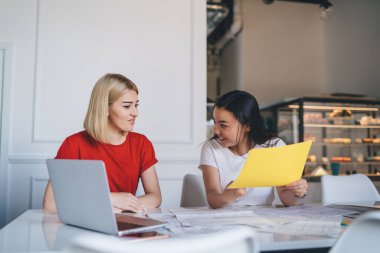 Gündelik giysiler içinde, masada oturmuş modern yaratıcı iş yerindeki belgeleri kontrol eden zeki ve çok kültürlü kadınlar.