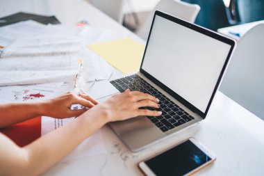 Yukarıdan klavyeye yazı yazan ve masadaki beyaz ekranlı, ofiste belgeleri olan bir kadın.