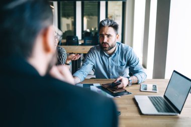 Sinirli erkek müdür çalışma saatlerini tartışıyor ve masada oturup iş toplantısına katılırken iş arkadaşıyla hata yapma konusunu tartışıyor. 