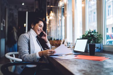Neşeli kadın danışmanlık yapmak için cep telefonu bağlantısını kullanıyor ve kahve dükkanındaki mesai saatleri boyunca doküman raporlarını tartışıyor. İnternet reklamları için ekran oluşturan dizüstü bilgisayar ağı.