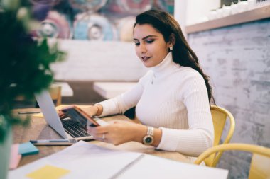 Beyaz kadın, bluetooth 'a bağlı akıllı telefon ve dizüstü bilgisayar teknolojisi ile medya dosyalarını paylaşıyor, özel ders sırasında cep telefonundan e-posta alan yetenekli bayan serbest yazar