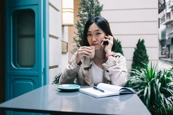 Mladá Asijská Žena Šálkem Kávy Sedí Stolem Mluví Smartphone Při — Stock fotografie
