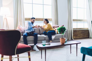 Genç etnik erkek ve kadın gündelik giysiler içinde kanepede dinleniyor ve cep telefonundan mesajlaşıyorlar.