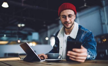Modern dijital cihaz kullanarak, tavan arasında bir bardak içecekle tabletin önünde oturan mutlu ve yakışıklı bir erkek.