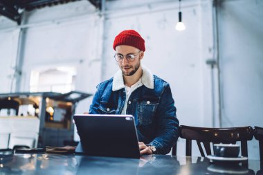 Çatı katında ekrana bakarken bilgi taramak ve aramak için modern dijital cihazda çalışan gündelik kıyafetlerle odaklanmış genç bir erkek.