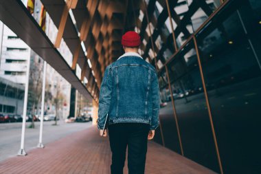 Kırmızı şapkalı, kot ceketli, tabletli ve şehir merkezindeki modern cam binanın önünden geçen...