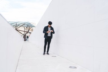 Modern tarz, ciddi, esmer ve etnik bir adam. Gündüz vakti sokak tünelinde dikilirken tablet üzerinde geziniyor.