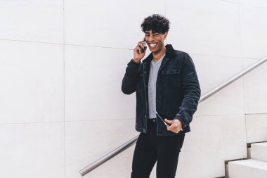 Neşeli Latin hipster 'ın yarım boy portresi cep telefonu görüşmeleri sırasında arkadaşlarıyla görüşürken kameraya gülümsüyor, akıllı telefondan telefon ediyor ve gülüyor.