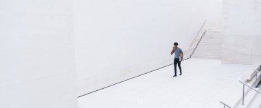 Beyaz iş merkezinde elinde belgelerle dolaşırken akıllı telefondan konuşan gündelik kıyafetlerle üst düzey etnik bir adamdan.