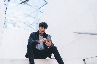 Beyaz modern binada merdivenlerde otururken kıvırcık saçlı, akıllı telefon kullanan afro-amerikalı genç adam şok oldu.