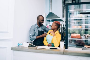 Kısa saçlı, neşeli, Afro-Amerikan genç bir kadın. Pasta dükkanındaki siyahi iş arkadaşıyla sohbet ediyor. Birbirlerine bakıyor.