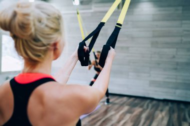 Sıska saçlı, spor elbiseli, ayakta duran ve spor salonunda kauçuk genişleticiyle egzersiz yapan zayıf bir kadının arka planı.