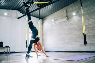 Siyah spor sutyen ve tayt giyen güçlü bir sporcunun spor salonundaki süspansiyon çalışmasında elleri yerde dururken tek bacağını kaldırması.