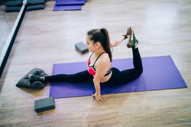 Spor elbiseli, spor kıyafetli, spor salonunun minderinde aynanın önünde uzanan genç bir kadın.