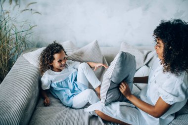 Yukardan neşeli bir çocuk, evinde kanepede yastıklı bir şekilde otururken güzel annesiyle eğleniyor.