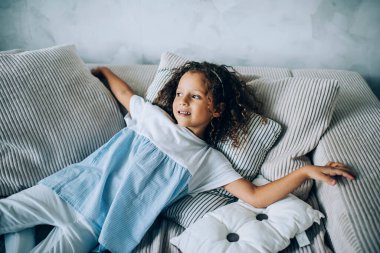 Yukardan gelen rahat, kıvırcık elbiseli çocuktan ev yastıklarında oynaşıp başka tarafa baktıktan sonra dinlenen.