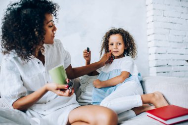 Evde kanepede bisküvi yerken bir fincan çay ve kurabiye ile sevimli çocuğun kirli yanaklarını temizleyen etnik anne.