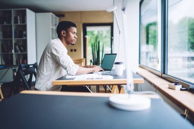 Milenyum programcısı birlikte çalışma alanında masa başında oturmuş web platformunu geliştirirken bilgi üzerine kafa yoruyor, Afrikalı Amerikalı erkek öğrenci çevrimiçi e-öğrenim sırasında düşünceli