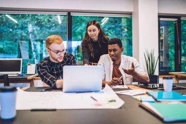Etkin yoğunlaşmış çok ırklı erkek ve kadın grup arkadaşları kütüphanede eğitim projesi üzerinde çalışırken laptoplarını paylaşarak ve sorunları çözerek canlı etkileşim içindeler.