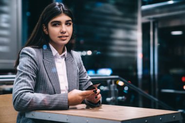 Kendine güvenen, resmi takım elbiseli bir kadın çalışan kafenin önünde oturuyor ve gözlerini başka yöne çeviriyor.