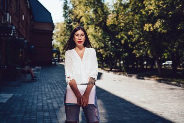 Şehir merkezinde öğrenim görmek ve poz vermek için klasik gözlüklü çekici bir kadının yarım boy portresi.