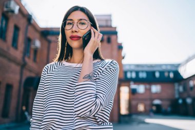 Gözlüklü çekici bir kızın yarı boy portresi. Şehir sokağındaki boş zamanlarında kameraya bakıyor. 4 g 'lik interneti telefonla kullanan güzel bir kadın.