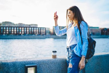 Kendine güvenen kadın blogcu cep telefonuyla güzel günbatımını çekiyor. Nehir köprüsünde yürüyor, şehri yeniden canlandırıyor, genç bayan seyahat blogcusu akıllı telefon kamerasıyla kentsel ayarların fotoğrafını çekiyor.