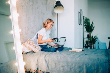 Gözlüklü, gözlüklü, akıllı telefon ve dizüstü bilgisayar kullanarak gülümseyen neşeli kadınların yan görüntüsü.