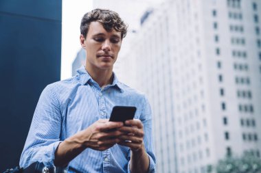 Yakışıklı, mavi tişörtlü genç adam New York 'un caddesinde ticari binanın önünde mobil sörf yapıyor. 