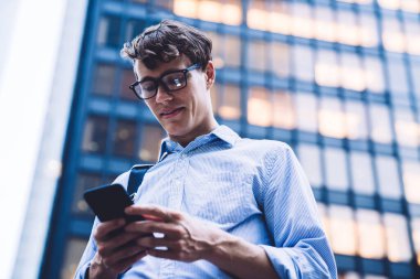 Modern cep telefonu kontrol sitesinde 4G kablosuz ağ kullanarak resmi olarak giyinmiş gururlu CEO 'nun bakış açısının altında, klasik gözlüklü bir adam online para transferi yaparken posta yazıyor.