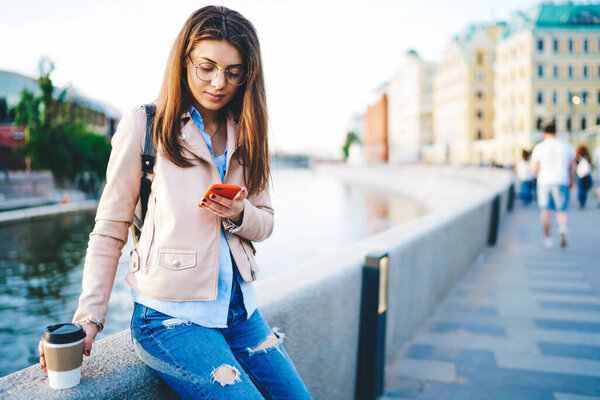 Пенсионерка в электронном виде читает сообщения и оповещения на мобильном телефоне, пьет кофе, чтобы поехать на речной мост, серьезная девушка-хипстер в повседневной одежде отправляет письма через приложение