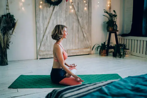 Caucasian woman calms brain minds with lotus yoga pose enjoying morning training in home apartment with loft design, wellbeing female increases awareness and attentiveness with padmasana exercise