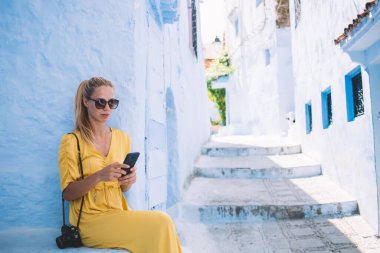 Günlük kıyafetleri ve güneş gözlükleriyle gezen genç bir kadın Fas 'ta dinlenen sosyal medyayı kontrol ediyor.