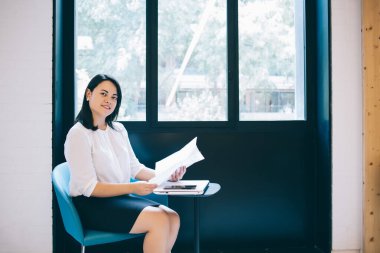 Zengin bir kadının portresi resmi olarak giyiniyor. Elinde evraklarla oturup mali verileri analiz ediyor. Kameraya bakıyor.