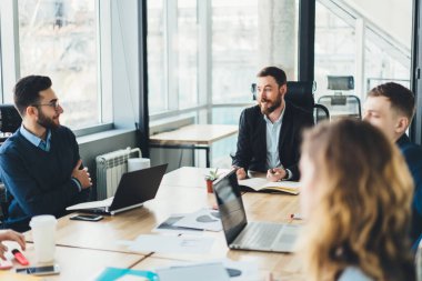 Modern ofisteki cihazlarla birlikte çalışma sırasında şirket geliştirme hakkında iletişim kuran başarılı genç bir grup çalışan.