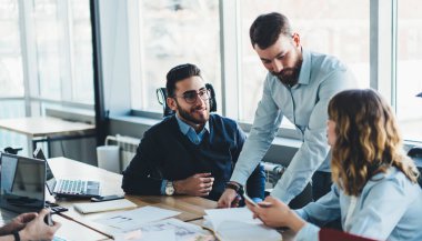 Modern ofisteki çalışma masasında belgelerle birlikte çalışırken resmi giyinmiş kadın ve erkek iş arkadaşlarının iletişiminden.