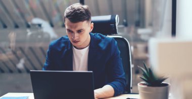 Şirket projesi ve modern işyerindeki bilgi analizi sırasında dizüstü bilgisayarı dikkatle izleyen ciddi konsantre genç erkek yöneticiler.