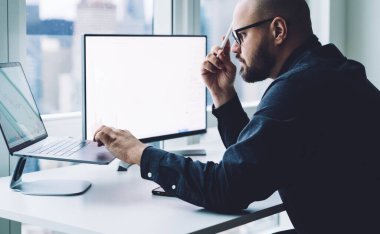 Modern ofiste bilgisayarla çalışırken dizüstü bilgisayar kullanan gözlüklü kel bir adamın kırpma kenarı görüntüsü. 