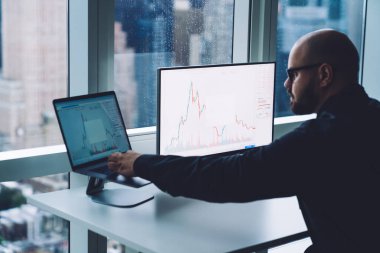 Ofiste çalışan bilgisayarlı ve grafikli bilgisayar kullanan gözlüklü profesyonel sakallı adamın yan görüntüsü 